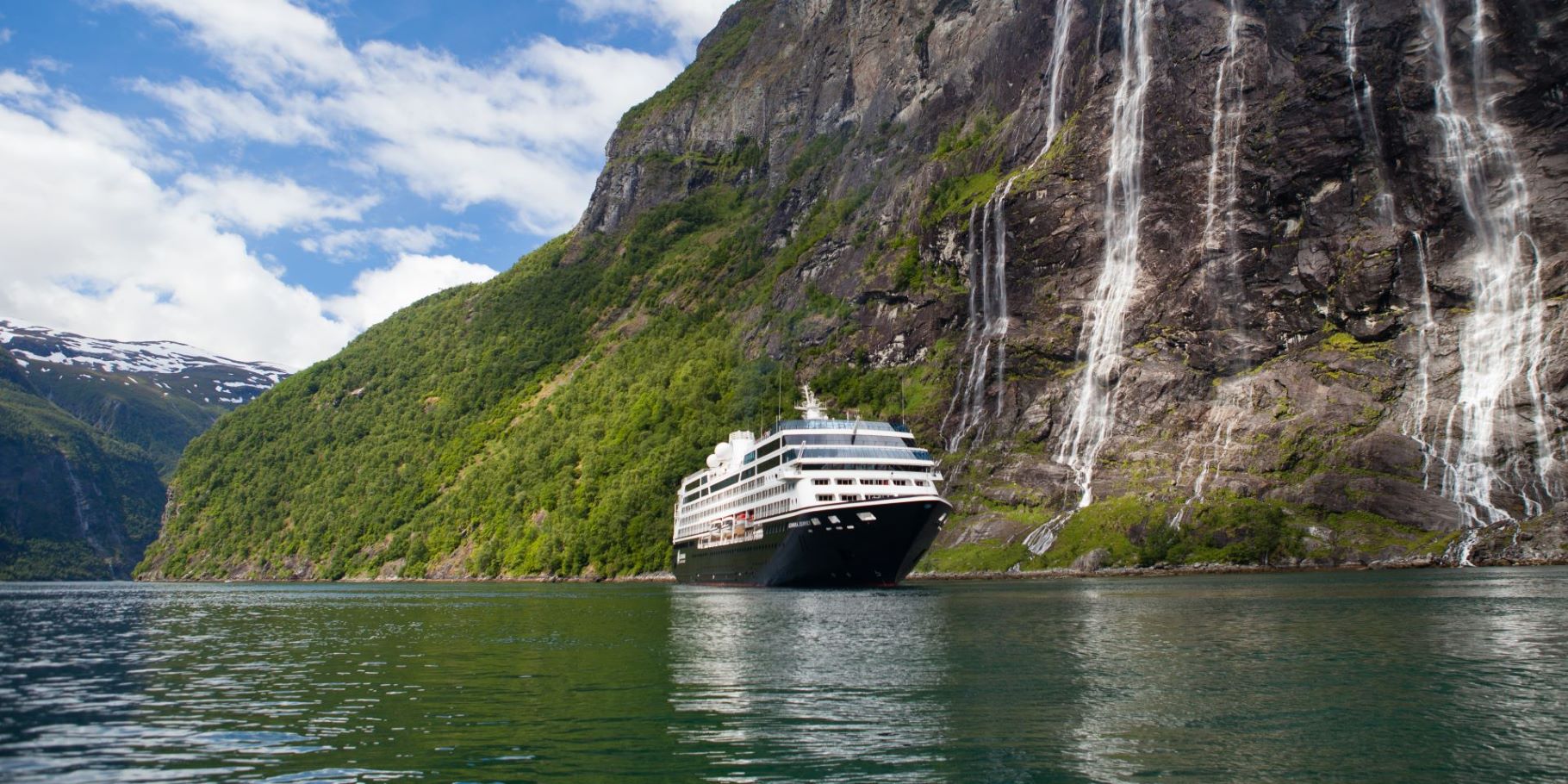 Azamara Journey sailing beside steep fjord cliffs and waterfalls